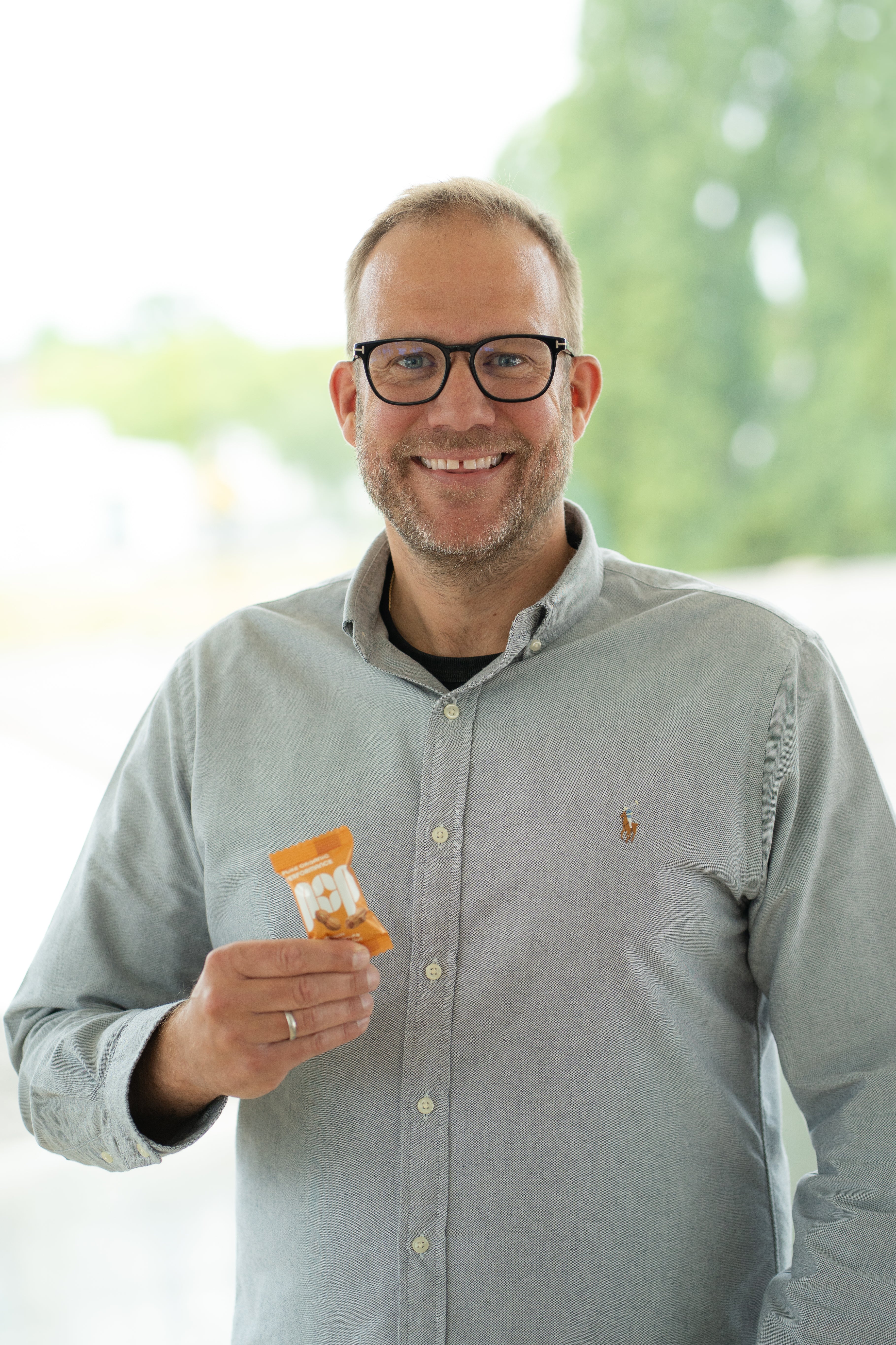 Porträt von Alexander Drees, Geschäftsführer der Sonnentracht GmbH und der Walter Lang GmbH, mit einem Salted Peanut Energy Ball in der Hand vor einem Fenster.