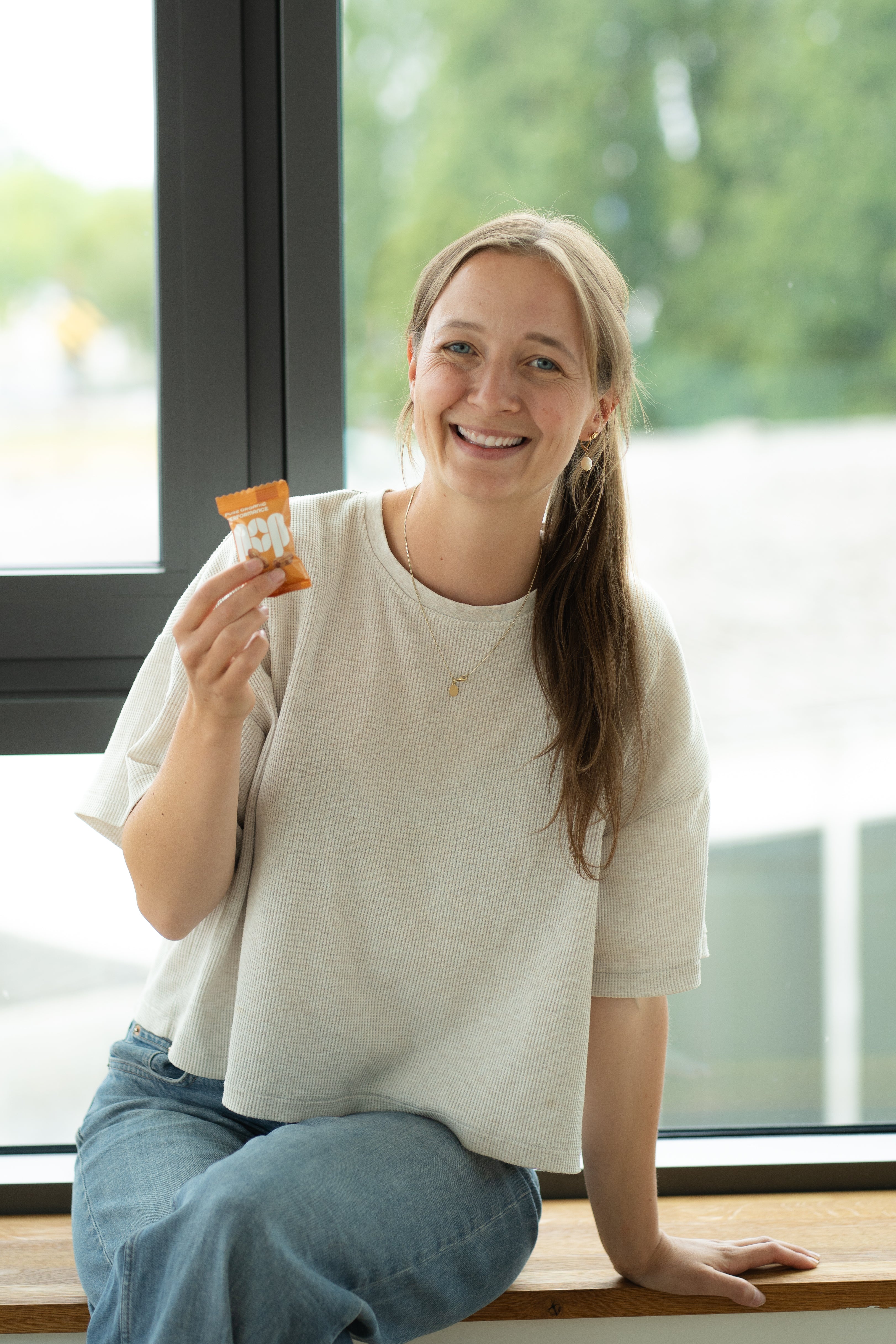 Porträt von Jana aus dem POP-Team mit Salted Peanut Energy Ball vor einem Fenster.