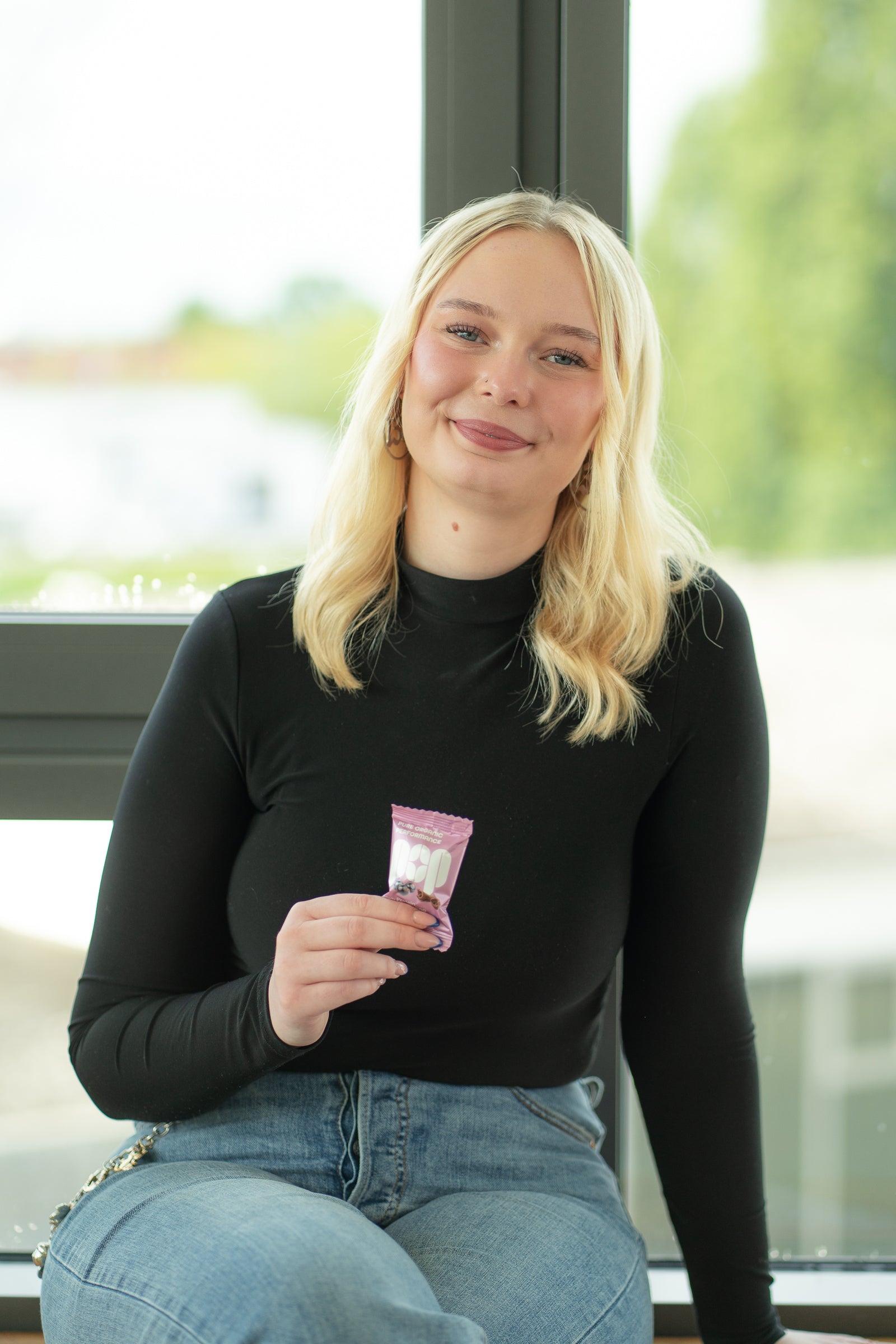 Porträt von Marlena aus dem POP-Team mit Cassis & Kakao Energy Ball in der Hand vor einem Fenster.